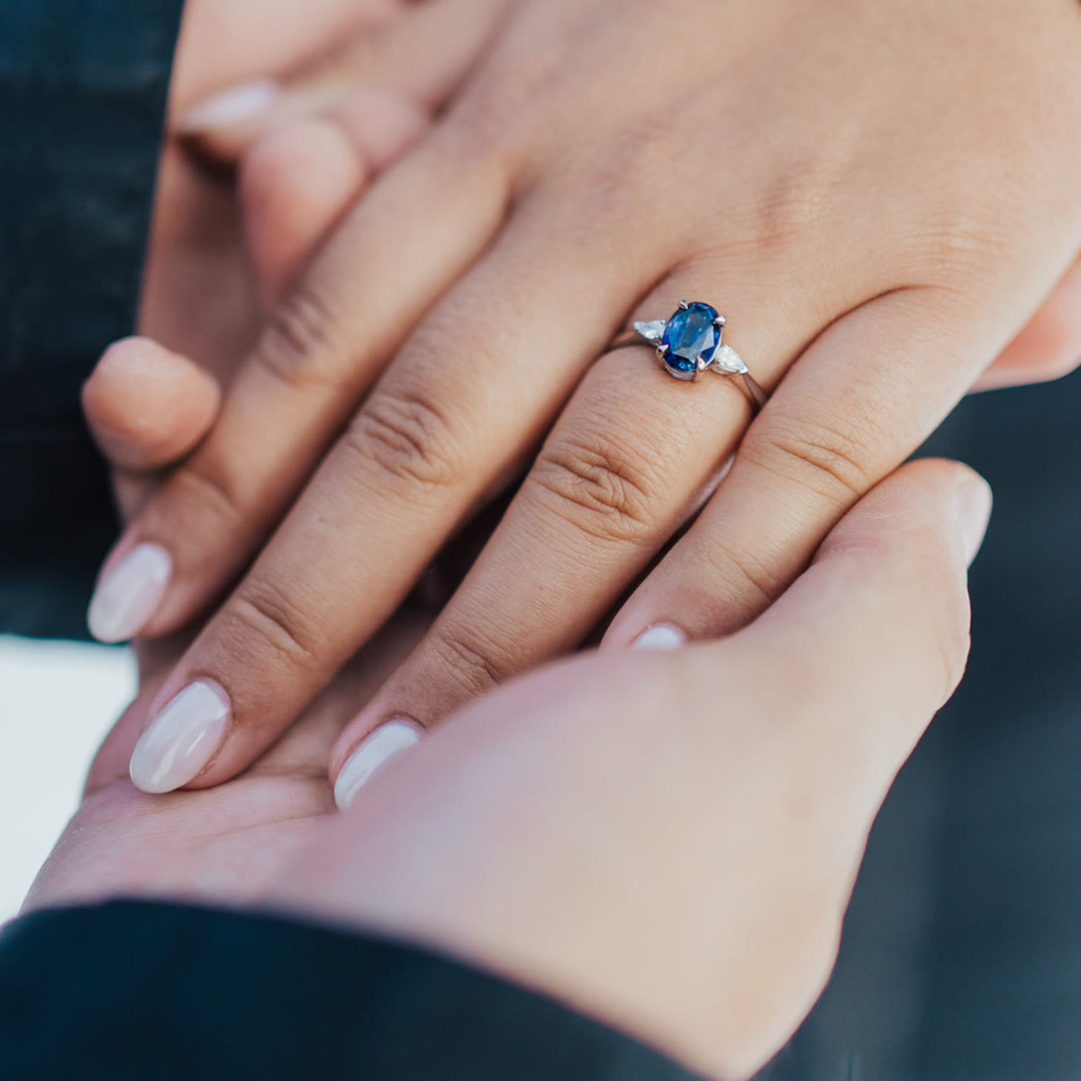 Blue sapphire engagement ring held in a partner's hands