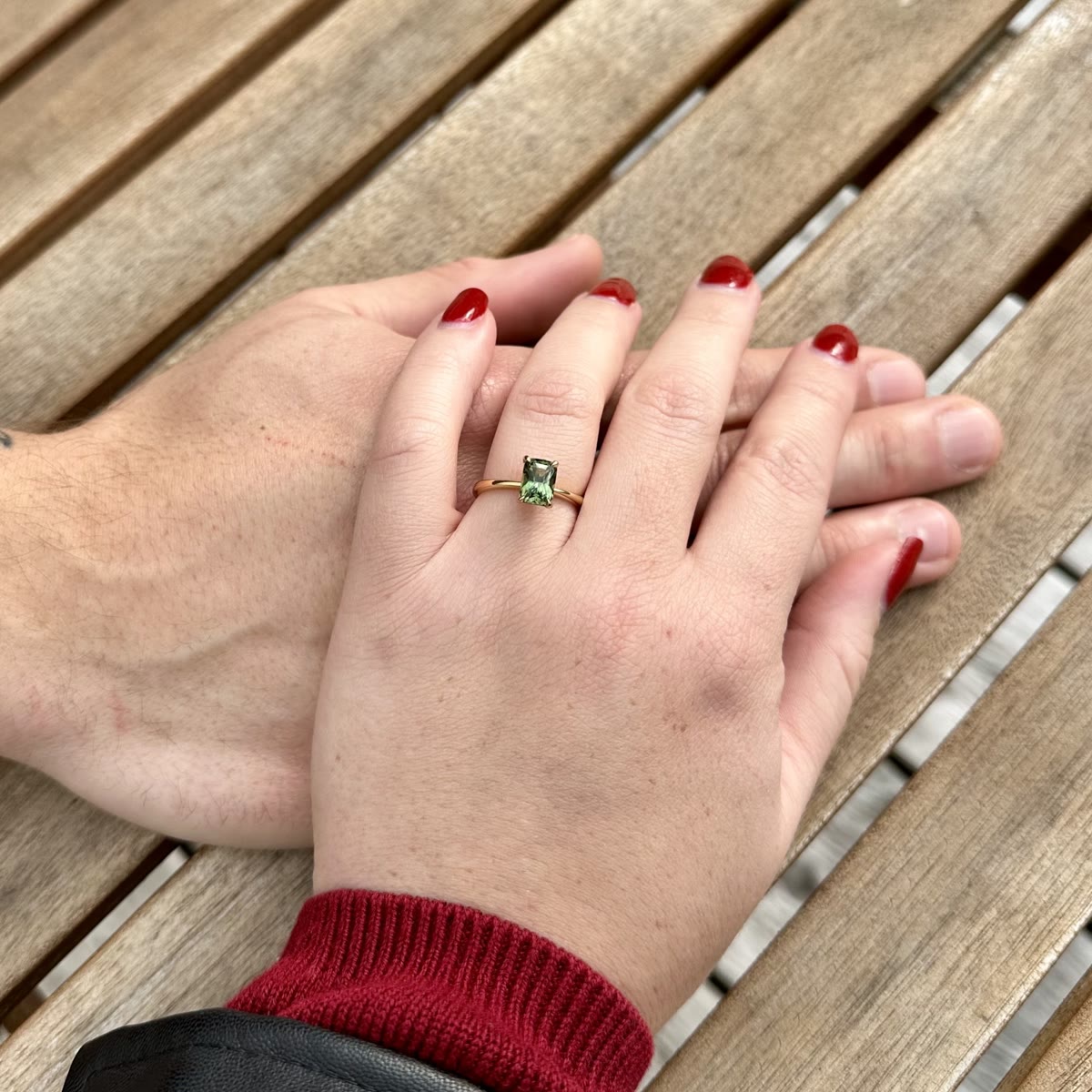 Green sapphire engagement ring on intertwined hands